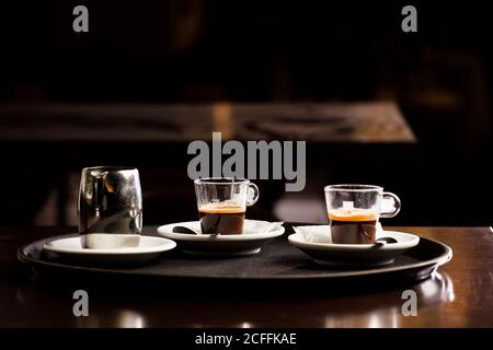 Zwei Tassen frisch gebrühten heißen Kaffees, auf dem Tablett des Kellners, auf dem Holztisch, im Café und freier Platz zur Dekoration. Stockfoto