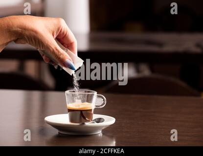 Weibliche Hand mit Zucker Umschlag in Kaffeetasse, auf Holztisch, in der Cafeteria und freien Raum für Dekoration gedumpt Stockfoto