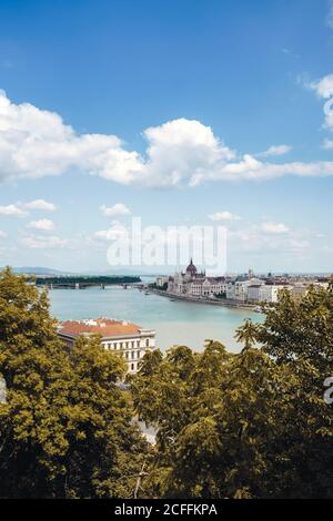 Ruhige Landschaft des ruhigen Flusses schwimmend entlang der Stadt mit Häusern Und Gärten unter hellen bewölkten Himmel in Budapest Stockfoto