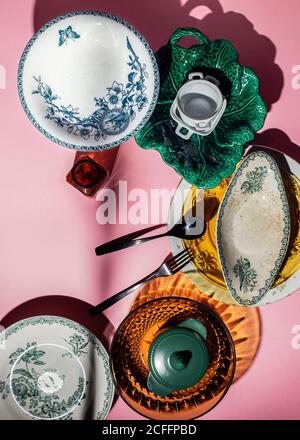 Draufsicht auf verschiedene Form mehrfarbigen Keramik und Glas vintage Utensil in Komposition mit Metallbesteck auf leuchtendem rosa Hintergrund In hellen Strahlen in der Küche Stockfoto