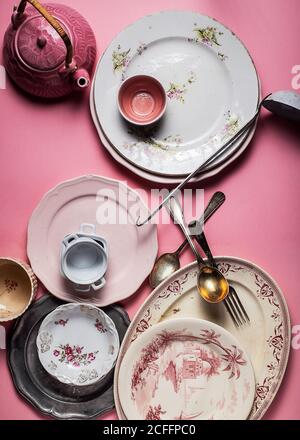 Draufsicht auf verschiedene Form mehrfarbigen Keramik und Glas vintage Utensil in Komposition mit Metallbesteck auf leuchtendem rosa Hintergrund In hellen Strahlen in der Küche Stockfoto
