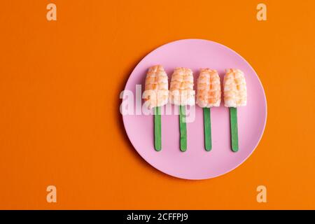 Draufsicht auf schmackhaftes Set von Ebi Nigiri Sushi mit Garnelen in Form von Eis serviert und auf den Teller gelegt Auf orangefarbenem Hintergrund im Studio Stockfoto