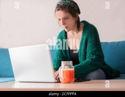 Von unten von weiblichen Freiberufler sitzen im Wohnzimmer an Tisch mit einem frischen Saft während der Arbeit online an Projekt Mit ihrem Netbook Stockfoto