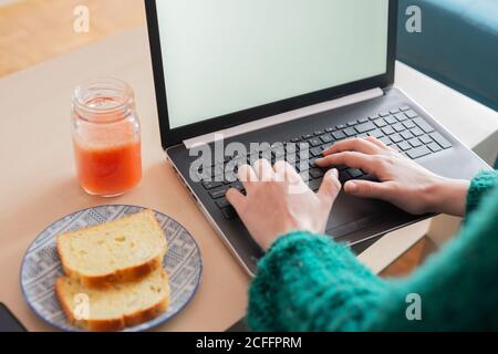 Von oben von weiblichen Freiberufler sitzen im Wohnzimmer an Tisch mit Toast und frischem Saft während der Arbeit online Projekt und Verwendung von Netbook Stockfoto