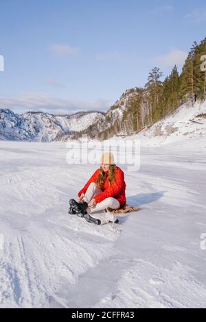 Frau auf Schnee sitzend und Stiefel wechselnd Stockfoto