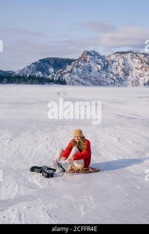 Frau auf Schnee sitzend und Stiefel wechselnd Stockfoto