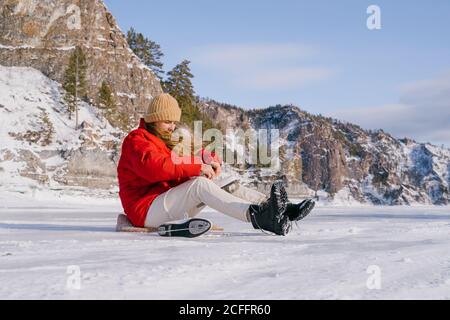 Frau auf Schnee sitzend und Stiefel wechselnd Stockfoto