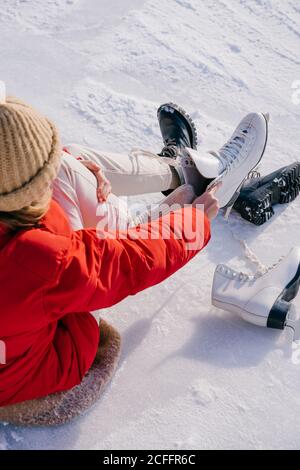 Frau auf Schnee sitzend und Stiefel wechselnd Stockfoto