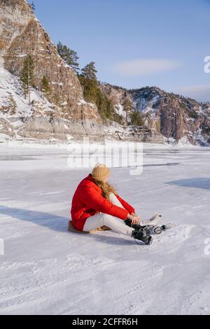 Frau auf Schnee sitzend und Stiefel wechselnd Stockfoto