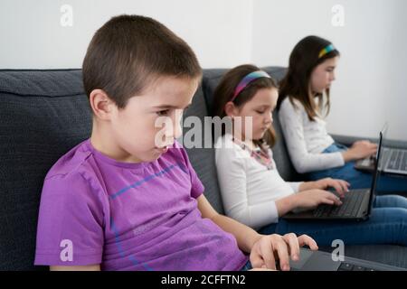 Gruppe von Kindern, die Laptops benutzen, während sie auf dem Sofa sitzen Zu Hause Stockfoto