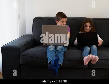 Gruppe von Kindern, die Laptops benutzen, während sie auf dem Sofa sitzen Zu Hause Stockfoto