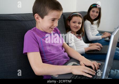 Gruppe von Kindern, die Laptops benutzen, während sie auf dem Sofa sitzen Zu Hause Stockfoto
