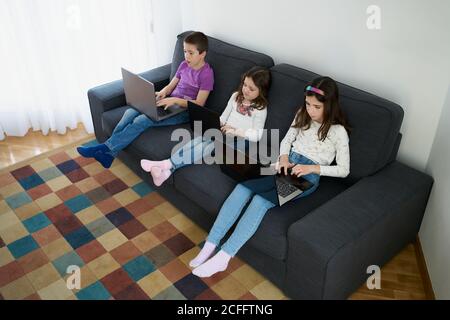 Gruppe von Kindern, die Laptops benutzen, während sie auf dem Sofa sitzen Zu Hause Stockfoto