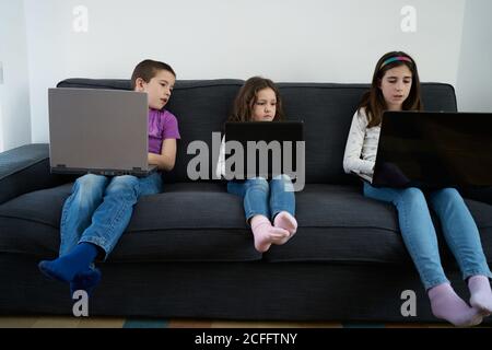 Gruppe von Kindern, die Laptops benutzen, während sie auf dem Sofa sitzen Zu Hause Stockfoto