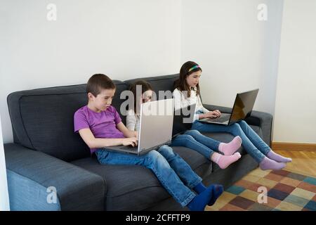 Gruppe von Kindern, die Laptops benutzen, während sie auf dem Sofa sitzen Zu Hause Stockfoto