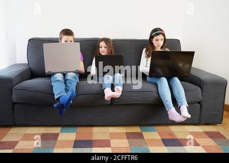 Gruppe von Kindern, die Laptops benutzen, während sie auf dem Sofa sitzen Zu Hause Stockfoto