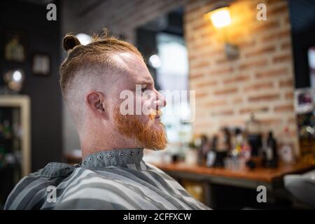 Seitenansicht des Rotschopf-Mannes, der in einem modernen Friseurladen sitzt und wartet Für den Friseur Stockfoto