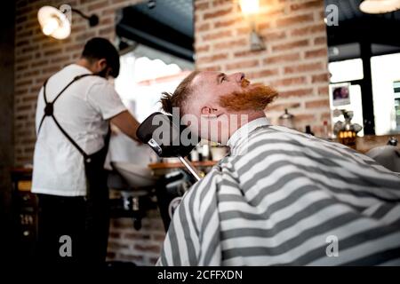Rotschopf Mann im Friseurladen wartet auf anonymen Friseur auf Der Hintergrund Stockfoto