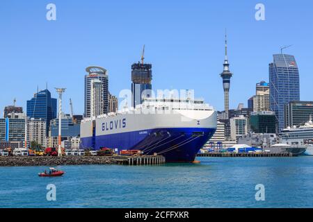 Die Skyline von Auckland, Neuseeland, vom Hafen aus. Im Vordergrund wird ein riesiges Transportschiff am Hafen entladen Stockfoto