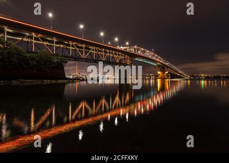 Die Auckland Harbour Bridge, Auckland, Neuseeland, beleuchtet in der Nacht mit hellorangefarbenem Licht Stockfoto