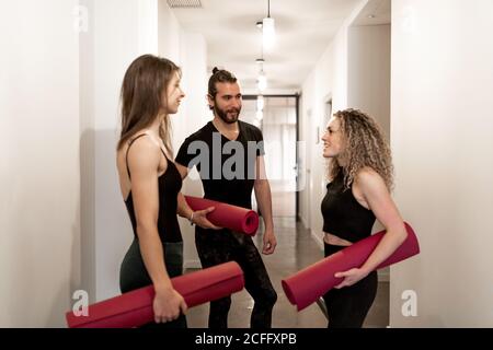 Junge Männer und Frauen mit Matten sprechen miteinander Während des Yoga-Trainings im Studio-Korridor stehen Stockfoto