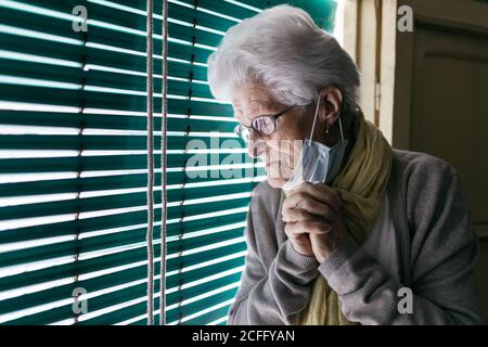 Ältere Frau, die während einer Pandemie in der Nähe des Fensters steht Stockfoto