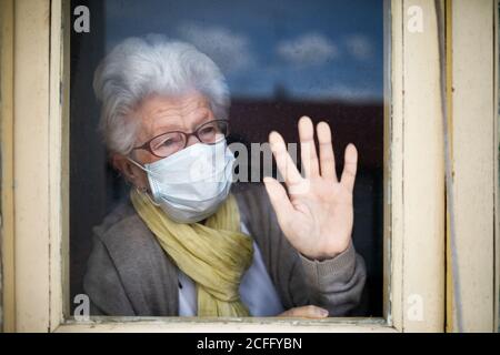 Ältere Frau mit Schutzmaske und Blick aus dem Fenster Stockfoto