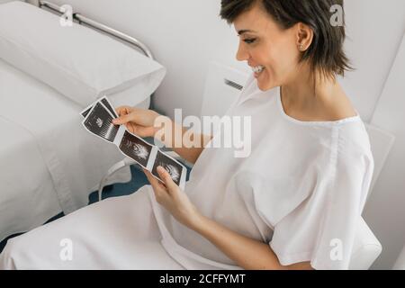 Von oben schwangere Frau inspiziert Sonogramm Bild während sitzen in Ein Stuhl auf der Station der modernen Fruchtbarkeitsklinik Stockfoto