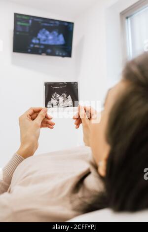 Nicht erkennbare schwangere Frau inspiziert Sonogramm Bild, während sie auf dem Bett liegen Auf der Station der modernen Fruchtbarkeit Klinik Stockfoto