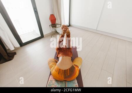 Aus der oberen Ansicht der afroamerikanischen anonymen jungen Frau, die im hellen Raum mit dem Kopf nach unten Yoga-Pose durchführt und die Hände auf der Matte streckt Stockfoto