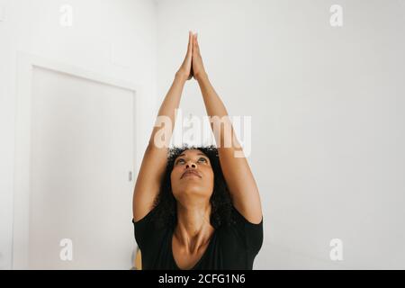 Afroamerikanische attraktive junge Frau, die im hellen Raum Yoga-Haltung mit gestreckten Armen auf Matte durchführt Stockfoto