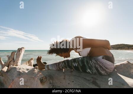 Seitenansicht der afroamerikanischen attraktiven jungen Frau, die am Strand eine Titibasana-Yoga-Haltung einnimmt Stockfoto