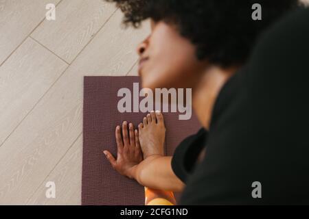 Von oben aus der Nahaufnahme der afroamerikanischen attraktiven jungen Frau, die zu Hause mit geschlossenen Augen auf einer Matte Yoga-Pose durchführt Stockfoto