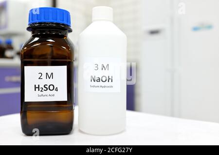 Selektive Konzentration von Natriumhydroxidbasis und Schwefelsäurelösung in braunen Glas- und Kunststoffflaschen in einem Chemielabor. Weißer Hintergrund Stockfoto