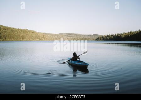 Silhouette einer anonymen Reisenden auf Kajak sitzen und rudern während der Reise auf ruhigen Fluss an wolkenlosen Tag im La Mauricie Nationalpark in Quebec, Kanada Stockfoto
