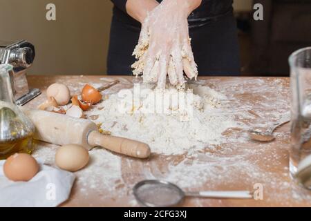 Anonyme Person in schwarzen Kleidern, die eine Vertiefung in Mehlmasse machen Mit der Hand zum Hinzufügen von Eiern beim Kochen von Teig für Pasta Zu Hause Stockfoto