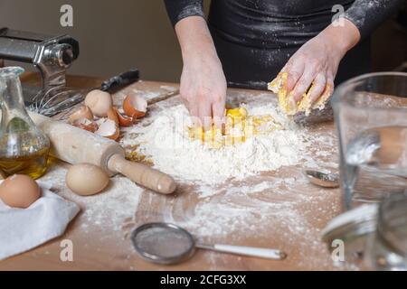 Anonyme Person in schwarzen Kleidern, die eine Vertiefung in Mehlmasse machen Mit der Hand zum Hinzufügen von Eiern beim Kochen von Teig für Pasta Zu Hause Stockfoto