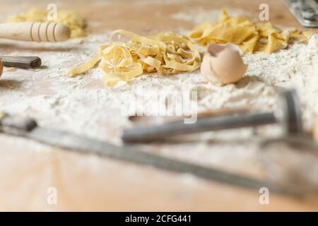 Rohe Streifen hausgemachter Pasta auf Holztisch mit bestreut Mehl neben Eierschalen und Küchenutensilien zu Hause Stockfoto