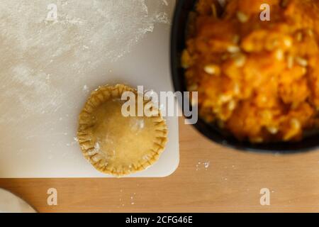 Draufsicht auf Schüssel mit köstlicher Füllung für Ravioli aus Kürbispüree und Nüsse auf dem Tisch neben einem Stück Teig Olivenöl Glas Mehl und Schneidebrett mit rohen Ravioli Stockfoto