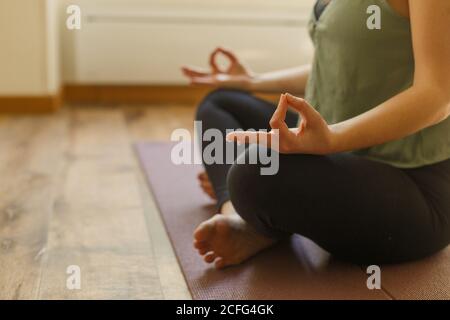 Seitenansicht einer anonymen Frau in Sportkleidung, die barfuß sitzt Boden und Yoga-Übungen in Padmasana mit Mudra-Geste Stockfoto