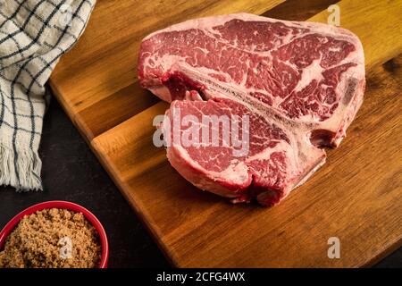 Foto von Porterhouse Steak auf einem Schneidebrett, mit einem würzigen braunen suger reiben auf der Seite, mit einem Küchentuch im Hintergrund Stockfoto