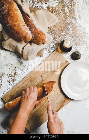 Von oben kochen das Ausschneiden des golden gebackenen Brotes auf hölzern Brett auf rustikaler Oberfläche Stockfoto