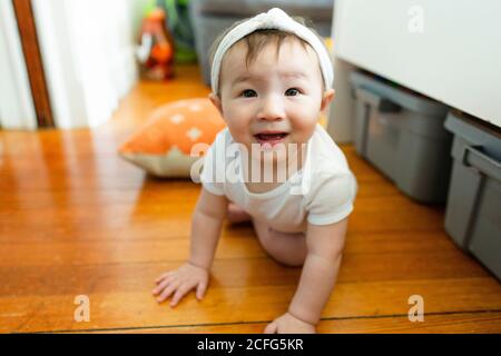 Neugieriges Baby macht Blickkontakt, während es zu Hause auf dem Boden kriecht Stockfoto