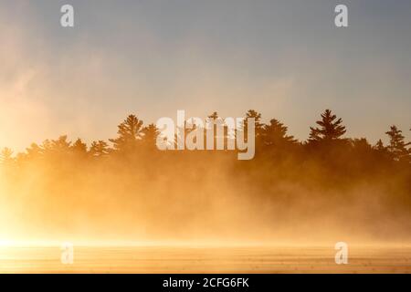Nebliger Morgennebel fängt die aufgehende Sonne auf bald Mountain Pond, Maine, ein Stockfoto