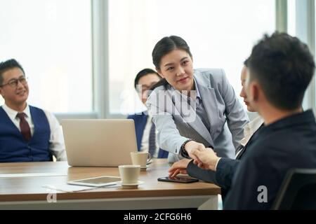 Junge asiatische Geschäftsfrau schüttelt Hände mit Geschäftsmann während des Treffens Stockfoto