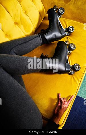 Von oben der Ernte nicht erkennbar schwarz Weibchen in Rollschuhe Auf gelbem Sofa liegend und mit Felsgestikte während des Aufenthalts Zu Hause während der Coronavirus-Sperre Stockfoto