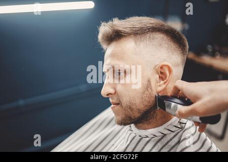 Barber scherzt den Bart zu Mann in Barbershop Framing Haarlinie. Elektrischer Rasierer, Vintage braun getönt Stockfoto