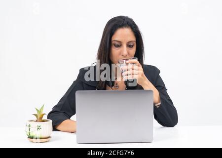 Porträt einer professionellen indischen Geschäftsfrau, die von ihrem Computer aus arbeitet, Freiberuflerin, Arbeit von zu Hause, Geschäftsfrau, die Wasser aus Glas trinkt Stockfoto