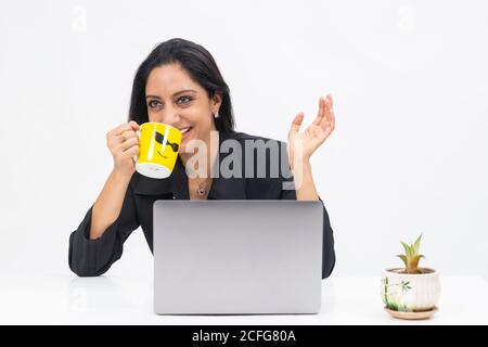 Porträt einer professionellen indischen Geschäftsfrau, die von ihrem Computer aus arbeitet, Freiberuflerin, Arbeit von zu Hause, Unternehmensdame, die Kaffeebecher hält und lächelt Stockfoto