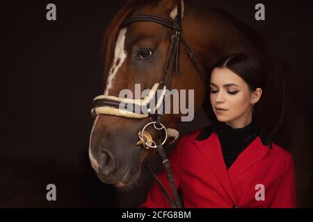 Reiter Jockey Frau Umarmungen mit braunem Pferd, schwarzer Hintergrund Stockfoto